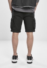 Black cargo shorts with rolled hems, side pockets, and a light texture, paired with black athletic shoes featuring white soles.