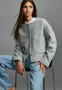 Grau melierte Wollmischung Jacke mit einem runden Kragen, Vordertaschen und Knopfverschluss, kombiniert mit hellblauem Denim. Glatte Textur.