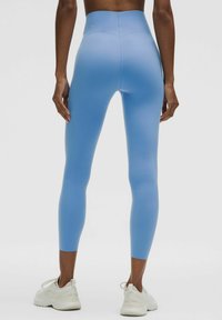 High-waisted yoga leggings in smooth, stretchy light blue fabric, fitted through the legs, paired with white athletic shoes.