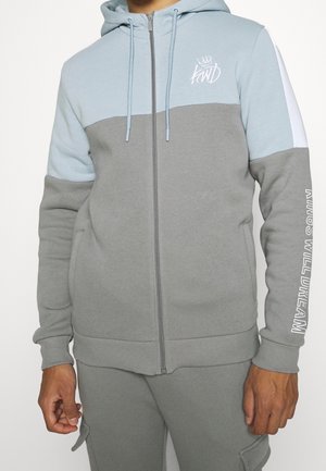 Szara i jasnoniebieska bluza z kapturem zapinana na zamek z przodu, z dwoma kieszeniami, ściągaczami na mankietach oraz napisem "KINGS WILL DREAM" na rękawie. Miękka w dotyku.