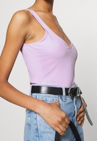 Débardeur lilas à côtes avec un décolleté en V profond, associé à un jean en denim clair taille haute et une ceinture en cuir noir avec une boucle argentée.