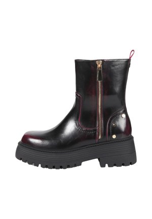 Bottine en cuir noir avec semelle épaisse, fermeture éclair latérale et petits clous décoratifs métalliques sur la zone du talon.