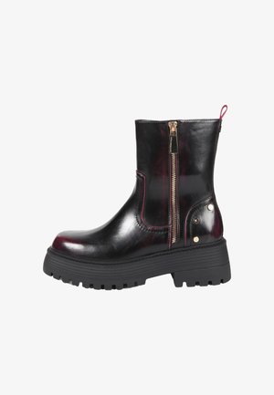 Bottine en cuir noir avec semelle épaisse, fermeture éclair latérale et petits clous décoratifs métalliques sur la zone du talon.