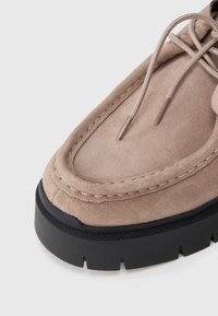 Chaussure en daim beige avec bout rond, couture contrastante et semelle en caoutchouc noire. Elle présente des lacets avec des embouts en métal.