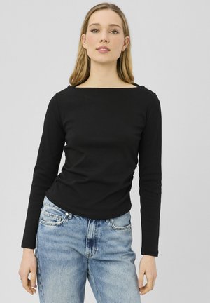 Haut noir à manches longues avec un col carré, coupe ajustée et texture douce ; associé à un jean bleu clair, doté d'une coupe classique.