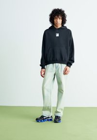 Black hooded sweatshirt with a small logo, light blue jeans, and black sneakers with blue accents. Smooth fabric and relaxed fit.