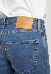 Blue denim jeans featuring a leather patch labeled "Levi Strauss & Co." at the back waist, with distinctive stitching and two back pockets.