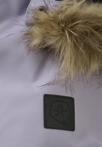 Lavendeltyg med en mjuk konstläderkant. Har ett svart rektangulärt logomärke sydd på tyget, med en enkel grafisk design.