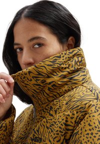 Gelbe Pufferjacke mit einem auffälligen schwarzen Tigerstreifenmuster, hohem Kragen und Reißverschluss, mit isolierter Textur und lockerer Passform.