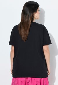 T-shirt nera in cotone con maniche corte, vestibilità comoda e scollatura rotonda. Indossata con una gonna rosa con volant, che mette in risalto il contrasto di colore e texture.