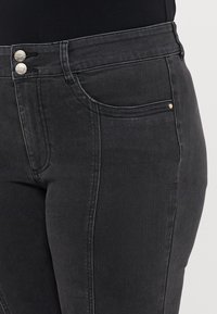 Svart denim högmidjade jeans med en figurnära design. Funktioner inkluderar två metallknappar, framfickor och subtila stygn detaljer.