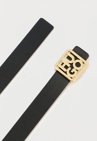 Czarny skórzany pasek z kwadratową złotą klamrą z wyciętymi literami tworzącymi napis "HUGO", gładka faktura, płaski kształt i minimalistyczny design.