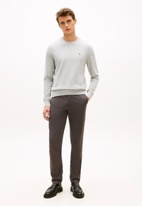 Szürke pamut pulóver bordázott mandzsettákkal és szegéllyel, sötétszürke nadrággal és fekete mokaszinnal párosítva. Minimalista dizájn logó részlettel.