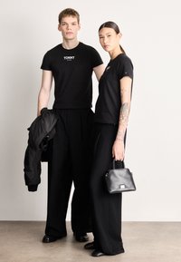 T-shirts pretas com o logo "TOMMY", calças pretas largas, uma jaqueta bomber e uma pequena mala preta. Tecido suave e design monocromático.