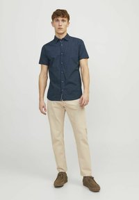 Camicia navy a maniche corte con pois bianchi, colletto a camicia, abbinata a pantaloni beige e scarpe marroni. Design semplice e aderente.