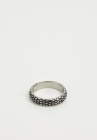 Bague en argent avec un motif texturé en écailles entourant l'anneau sur fond blanc uni.