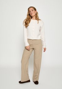 Helles rosa enges Cardigan mit Rundhalsausschnitt und Knopfverschluss, kombiniert mit beigen weit geschnittenen Hosen und braunen Schuhen. Gesamte glatte Textur.