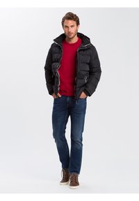 Czarna kurtka puchowa z zamkiem błyskawicznym, kapturem i bocznymi kieszeniami, noszona na czerwonym swetrze i niebieskich dżinsach, w połączeniu z brązowymi butami.