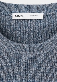 Gros plan du col d'un pull en maille bleu et blanc avec une étiquette blanche indiquant la marque MNG et la taille EU-USA M, MEX M.