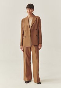 Dobbeltbrystet brun uldblazer med to forlommer, parret med matchende brede bukser. Minimalistisk design og glat tekstur.