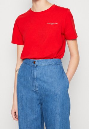 Rød bomulds T-shirt med rund halsudskæring og korte ærmer, der har et lille hvidt logo på venstre bryst. Sammen med højtaljede blå denimbukser.