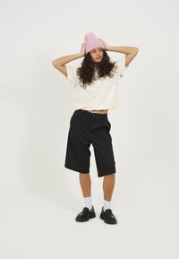 Black tailored shorts, relaxed fit; cream oversized t-shirt. Pink knitted beanie with pom-pom. Black loafers with thick soles.