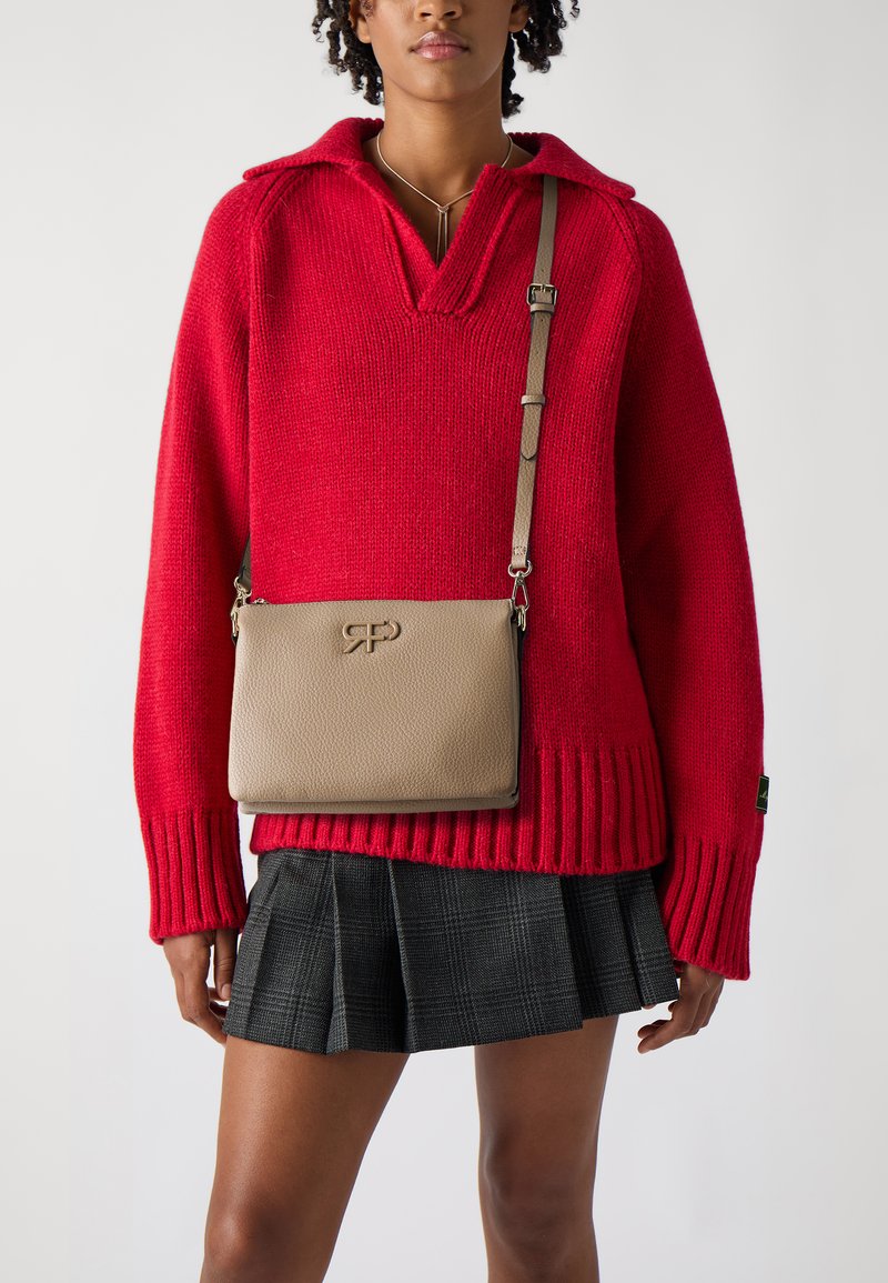 Beżowa skórzana torba na ramię o teksturowanym wykończeniu i wytłoczonym logo, zestawiona z czerwoną swetrem z dzianiny i plisowaną czarną spódnicą w kratę.