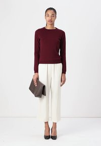 Bordeaux striktrøje med rund halslinje, cremefarvede vide bukser, sorte høje hæle og en foldet brun clutch-taske. Ensfarvet baggrund.
