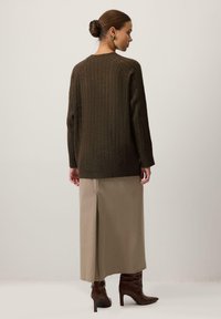 Olīvu zaļš ribotu džemperis ar brīvu piegriezumu, apvienots ar bēšu midi svārkiem ar aizmugures šķēlumu un brūnām zābaku kurpēm uz papēža.