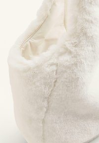 Vit fuskpälsväska med en mjuk textur. Rundad form med en sömdetalj och ett innerfoder, lämplig för att bära föremål.