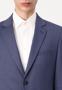 Blazer azul marino con tejido texturizado, cierre de un solo botón y un bolsillo en el pecho, combinado con una camisa blanca de botones.
