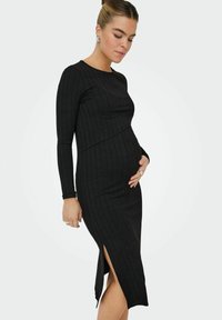 Vestito lungo nero a maniche lunghe con silhouette aderente e spacco laterale, realizzato in tessuto elastico, progettato per comfort e stile.