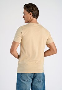 Beige bomullströja med korta ärmar, rund halsringning och subtila sömmar i sidan, tillsammans med bleka blå denimjeans.