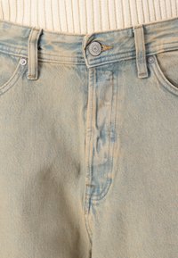 Vaqueros de mezclilla azul claro con cintura alta, textura desgastada, diseño estándar de cinco bolsillos y cierre de botón metálico en la cintura.