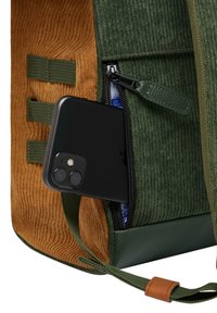 Zaino in corduroy verde e marrone con una tasca con cerniera. Un smartphone nero è parzialmente visibile nel compartimento. Presenti dettagli in pelle.
