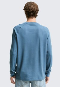 Blauses Langarmshirt aus strukturiertem Stoff, runder Ausschnitt und Raglanärmel. Mit einem dezenten Logo am Bündchen und lockerer Passform.