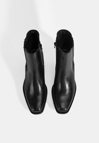 Bottes cheville en cuir noir avec un bout pointu élégant, des fermetures éclair latérales et des détails texturés à l'arrière. Fini lisse et matériel minimal.