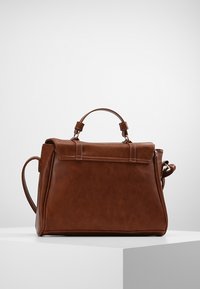 Ruskea nahkainen käsilaukku, jossa on jäsennelty muotoilu, yläkahva ja irrotettava olkahihna. Ominaisuuksiin kuuluu sileä pinta ja minimaalinen varustelu.