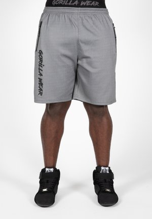 Grijze sportbroekjes met een mesh-textuur, elastische tailleband, zijritsen en "GORILLA WEAR" gedrukt op het linkerpijpje. Zwarte hoge sneakers.