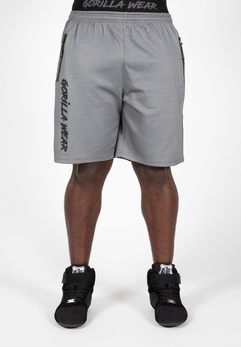 Grijze sportbroekjes met een mesh-textuur, elastische tailleband, zijritsen en "GORILLA WEAR" gedrukt op het linkerpijpje. Zwarte hoge sneakers.