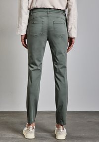 Pantaloni verde chiaro a vestibilità slim, dotati di due tasche posteriori e una texture liscia, abbinati a sneakers bianche e argentate.