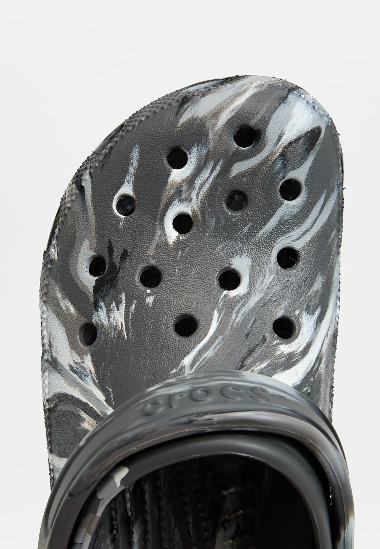 Czarno-białe crocsy w wzory z fakturowaną powierzchnią, z wieloma otworami wentylacyjnymi i zakrzywionym paskiem na pięcie.
