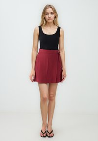 Zwarte geribbelde tanktop gecombineerd met een bordeauxrode geplooide mini rok, met een zijstrikdetail en een gladde textuur. Zwarte flip-flops maken de look af.