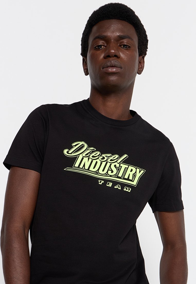 Czarna koszulka z krótkim rękawem z wyraźnym zielonym graficznym wzorem "Diesel INDUSTRY TEAM" na przodzie. Wykonana z miękkiej bawełny.