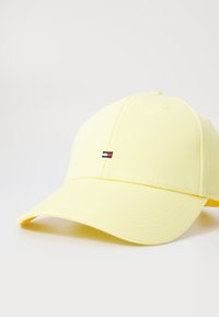 Casquette de baseball jaune en tissu avec un visière incurvée. Elle présente un petit logo brodé avec des rayures rouge, blanc et bleu à l'avant.