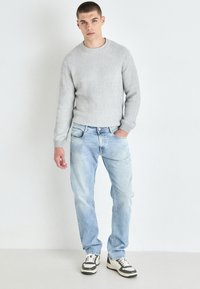 Grå ribbestrikket genser med rund hals, lyseblå falmede jeans og sneakers med lave topper som har svart og hvit detaljer. Uformell passform.