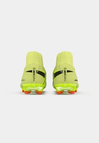 Para neonyellowowych korków do piłki nożnej z czarnymi logotypami Nike w kształcie smoka i czerwonymi korkami, widok z tyłu na białym tle.