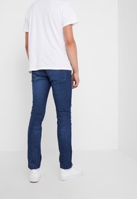 Jeans de denim en azul oscuro con un corte ajustado, combinados con una camiseta blanca básica y zapatillas blancas. Textura suave, diseño minimalista, sin patrones.