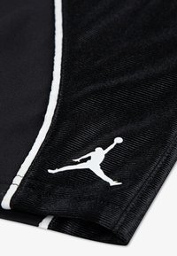 Μαύρο αθλητικό ύφασμα με υφή, με λευκό λογότυπο Jumpman και μια αντίθετη λευκή ρίγα κατά μήκος της άκρης.