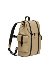 Beige vanntett ryggsekk med svarte detaljer, justerbare stropper, frontlomme, klaffelukk og forsterkede kanter for holdbarhet.